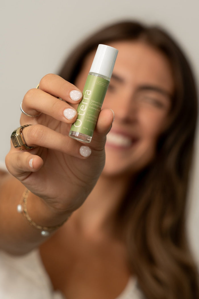Une femme sourit en tenant le sérum contour des yeux lumineux O'terra, un soin à la caféine pour un regard frais et réveillé.