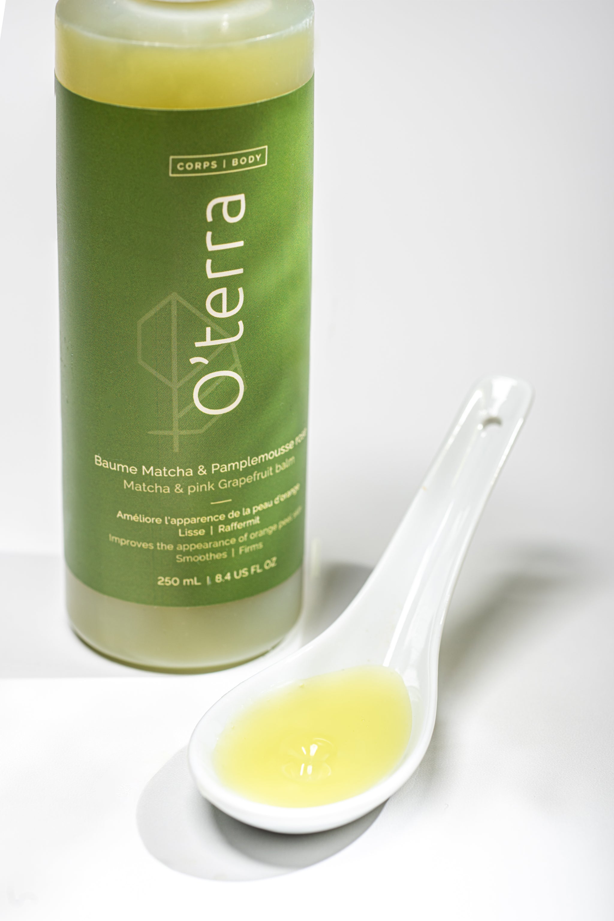 Bouteille du baume pour le corps naturel O'terra avec une cuillère blanche montrant la texture onctueuse au matcha et pamplemousse rose.