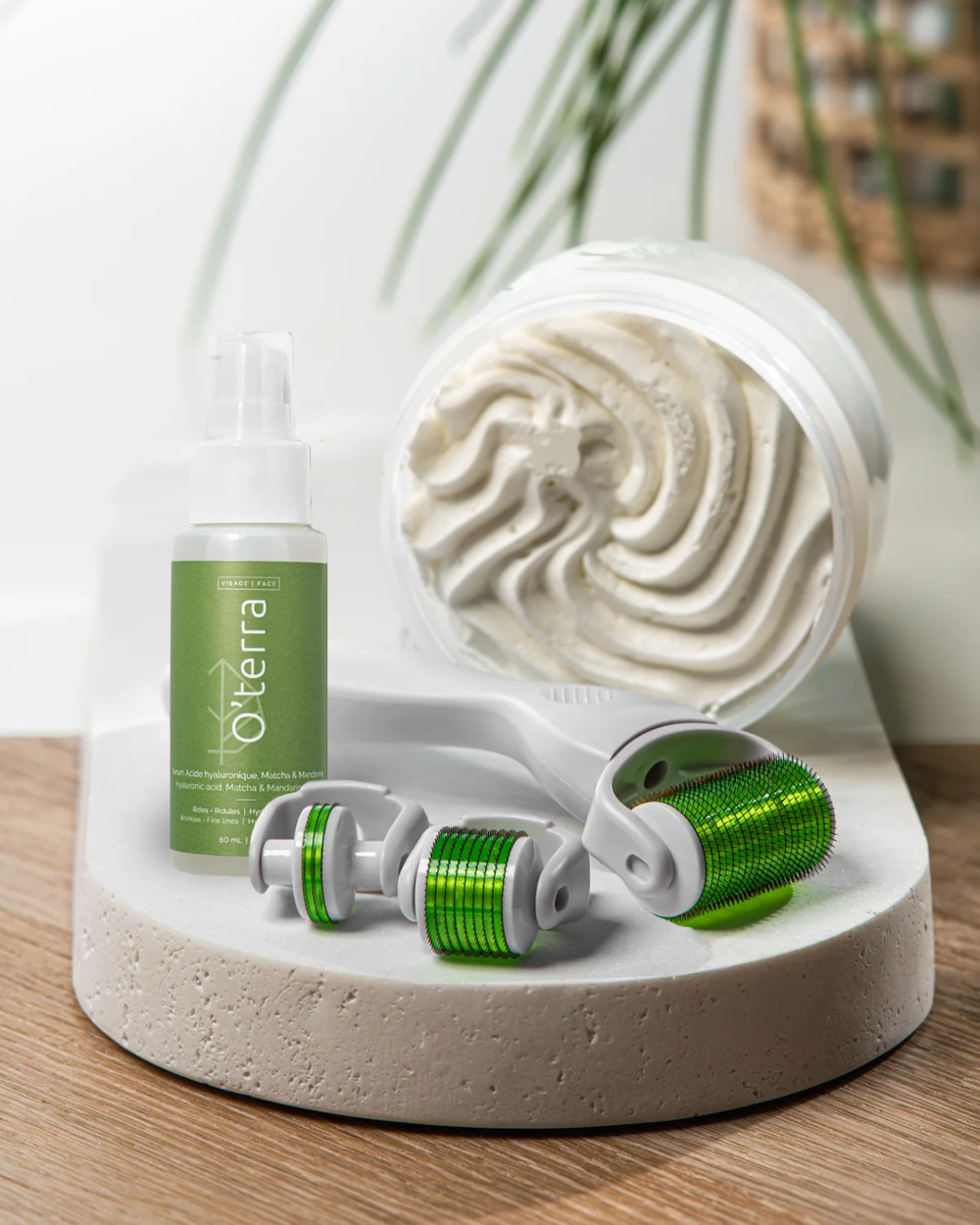 Ensemble complet O'terra sur un plateau en pierre comprenant le Dermaroller 3 en 1, le sérum visage à l'acide hyaluronique et un pot ouvert de beurre fouetté corporel.